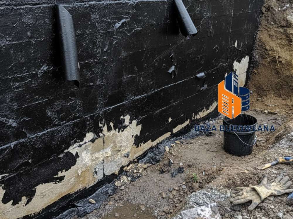 Prace przy hydroizolacji fundamentów z widoczną warstwą izolacji chroniącej ściany piwnicy przed wilgocią.